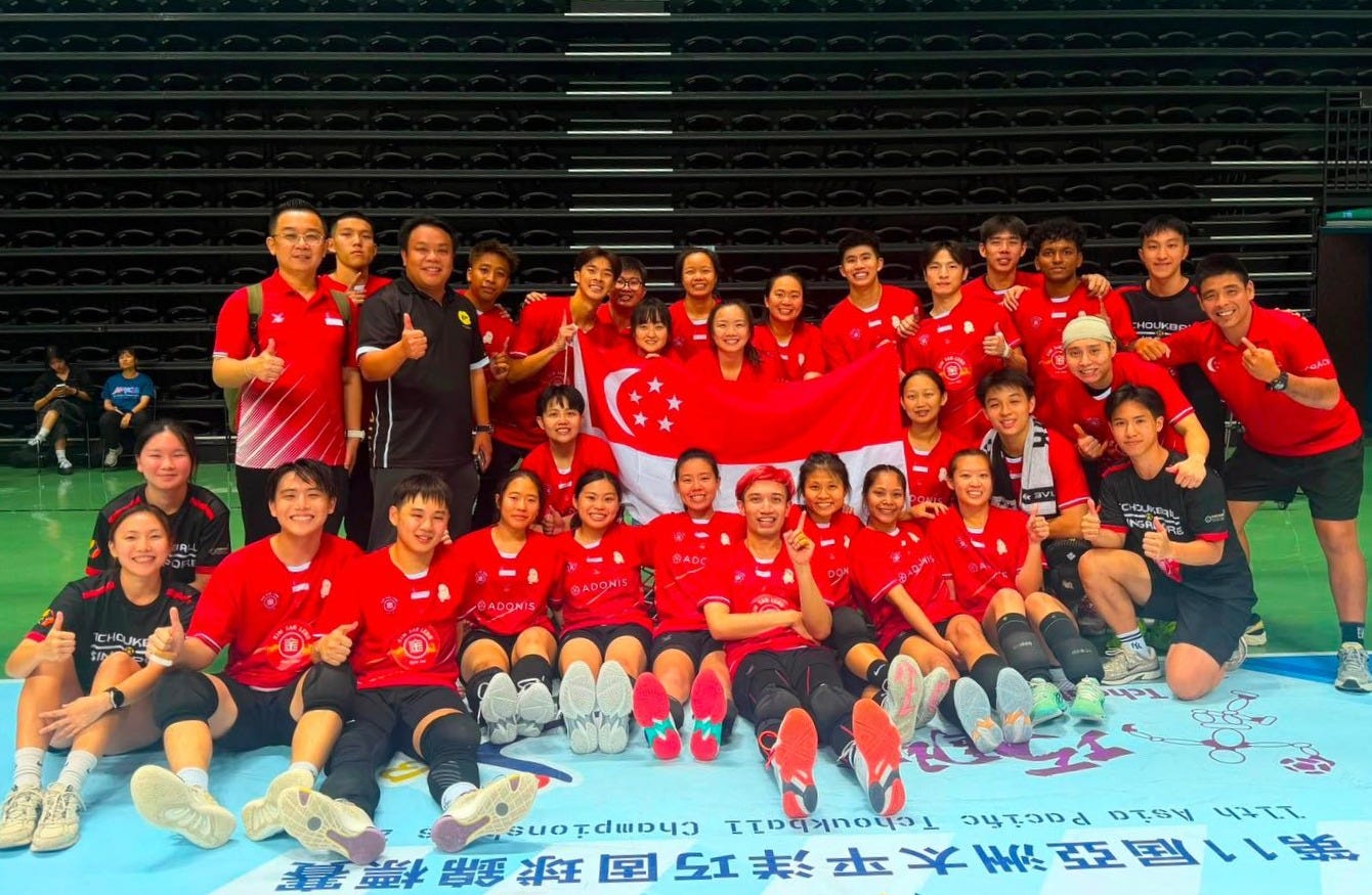 the Singapore national tchoukball squad poses together on an indoor sports court following their success at the Asia Pacific Tchoukball Championships (APTC 2026). The players and coaching staff, dressed in red and black team uniforms, smile for a group photo while proudly holding up the Singapore national flag. The court floor features tournament branding reading "11th Asia Pacific Tchoukball Championships," visually capturing Singapore’s gold and bronze medal finishes in the sport. the Singapore national tchoukball squad poses together on an indoor sports court following their success at the Asia Pacific Tchoukball Championships (APTC 2026). The players and coaching staff, dressed in red and black team uniforms, smile for a group photo while proudly holding up the Singapore national flag. The court floor features tournament branding reading "11th Asia Pacific Tchoukball Championships," visually capturing Singapore’s gold and bronze medal finishes in the sport.