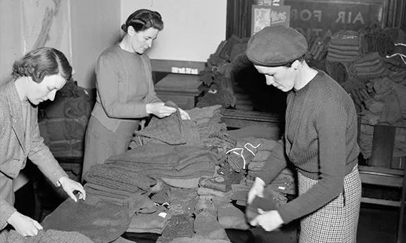 Black-and-white photograph of women packing knitted items into boxes, Wellington, New Zealand, 23 July 1945.