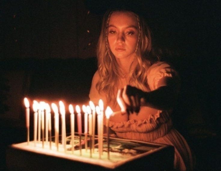 This may contain: a woman sitting in front of a cake with lit candles