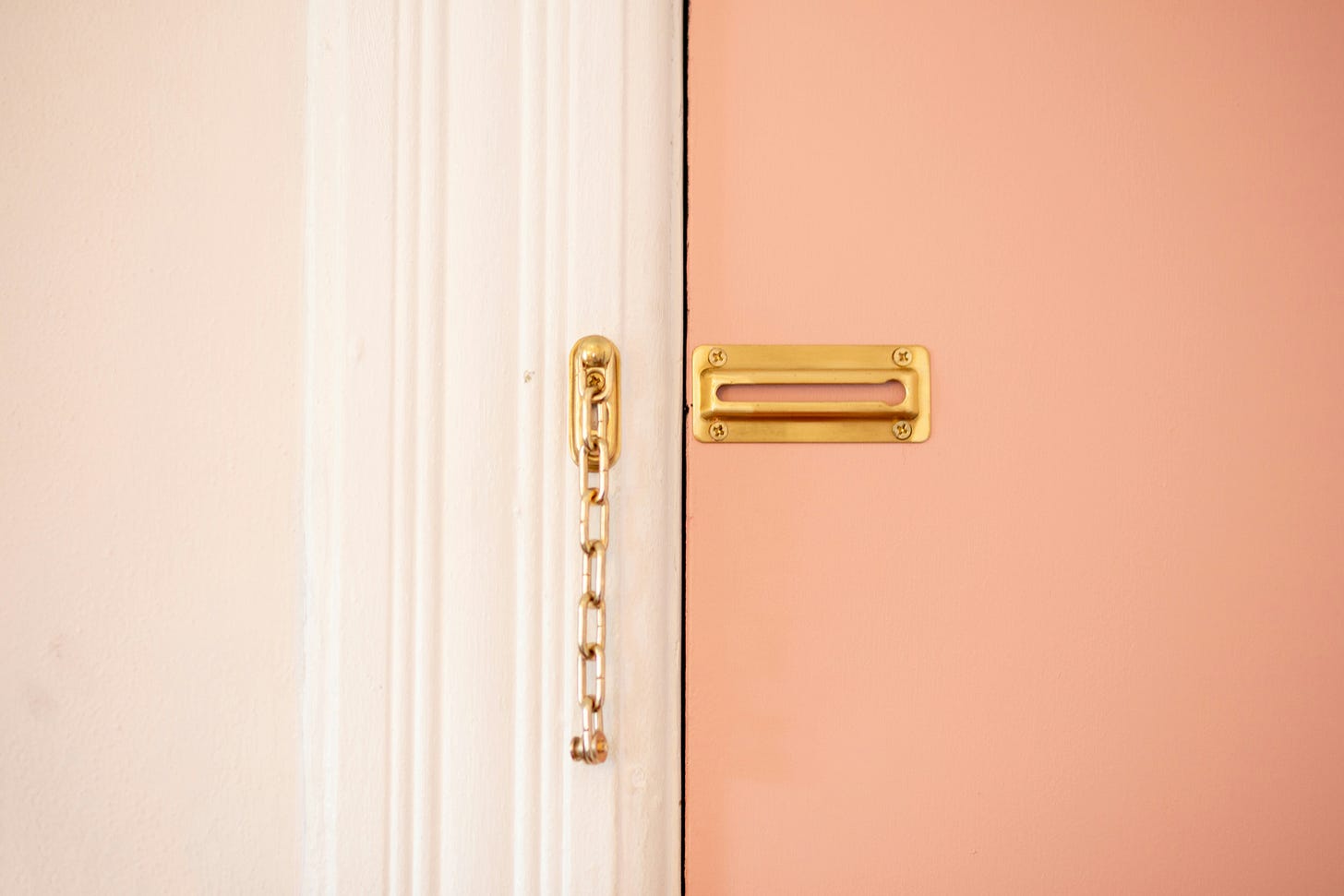 Photo of a portion of a closed pink door with a brass chain latch hanging unlocked
