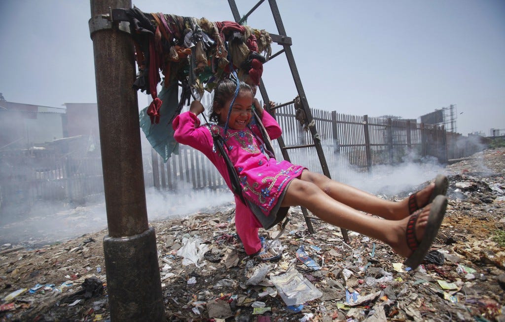 Sana, a five-year-old girl, plays on a cloth sling hanging from a signalling pole as smoke from a garbage dump rises next to a railway track in Mumbai in 2012. Photo by Vivek Prakash/Reuters