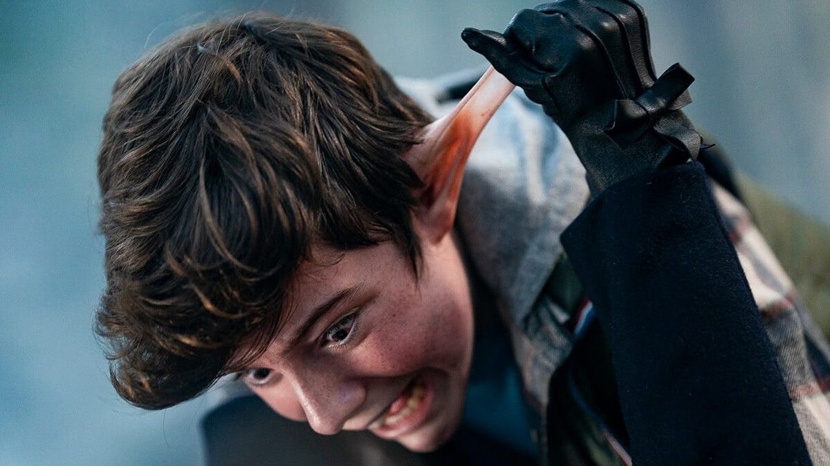 Close-up of a boy grimacing as M3GAN pulls his ear with a gloved hand. Close-up of a boy grimacing as M3GAN pulls his ear with a gloved hand.