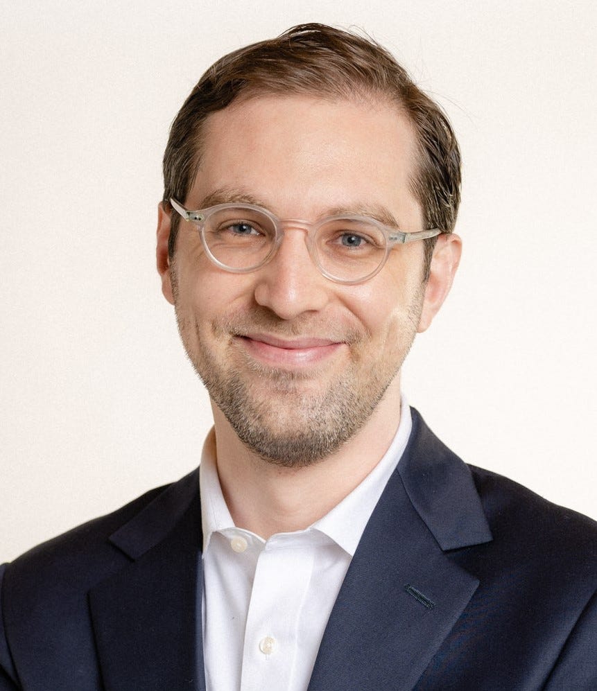 A person in a suit and glasses

AI-generated content may be incorrect.