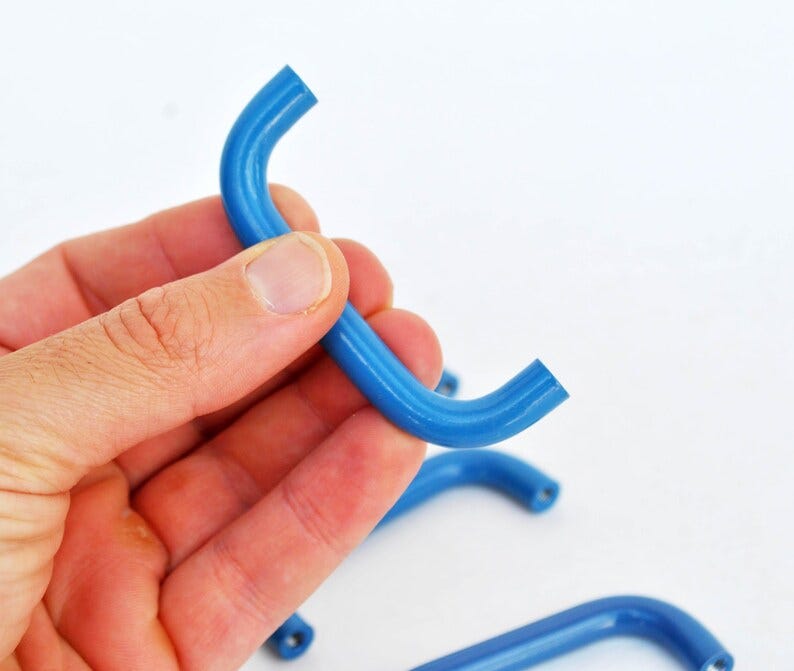 May include: Close-up of several curved, bright blue metal handles. The handles are in a semi-circle shape, with a smooth, glossy finish. The background is plain white.