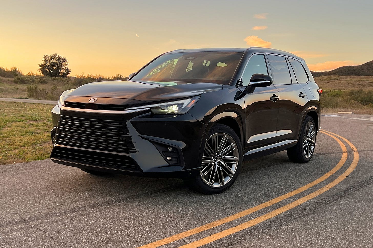 A black 2024 Lexus TX is parked on a road at sunset near the Santa Monica Mountains.