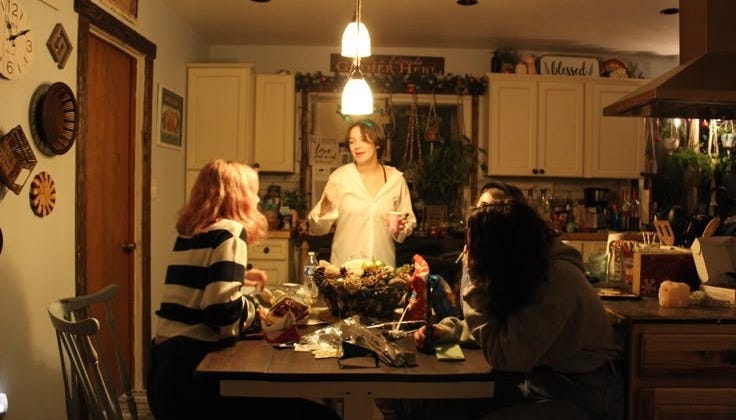 This may contain: a group of people sitting around a kitchen table with food on the counter and in front of them