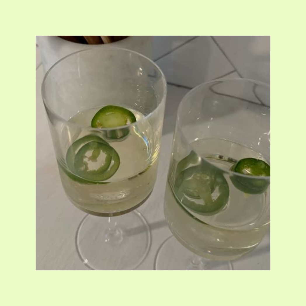 A photo of 2 glasses of white wine with jalapeños in them.