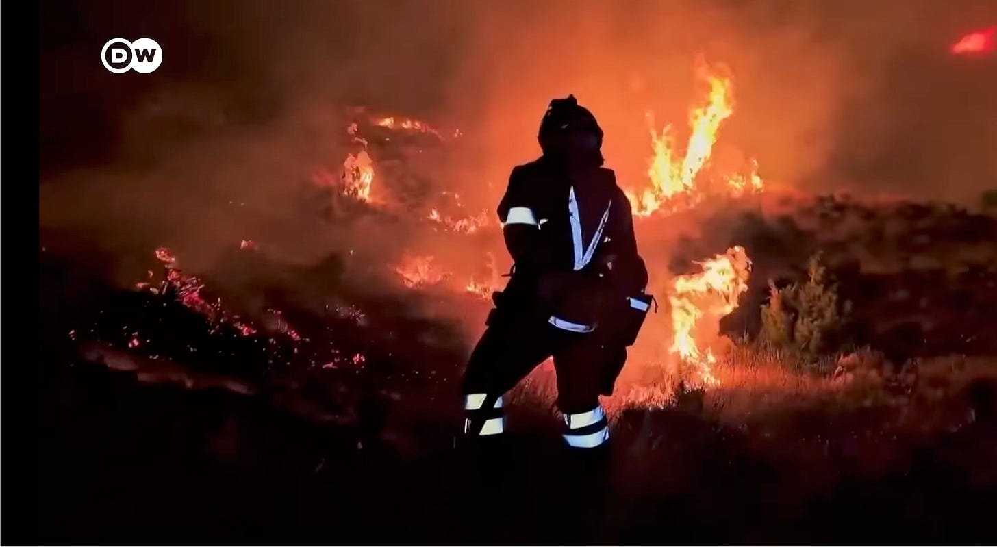 Night image. Firefighter, back to the camera in front of a fierce orange blaze.