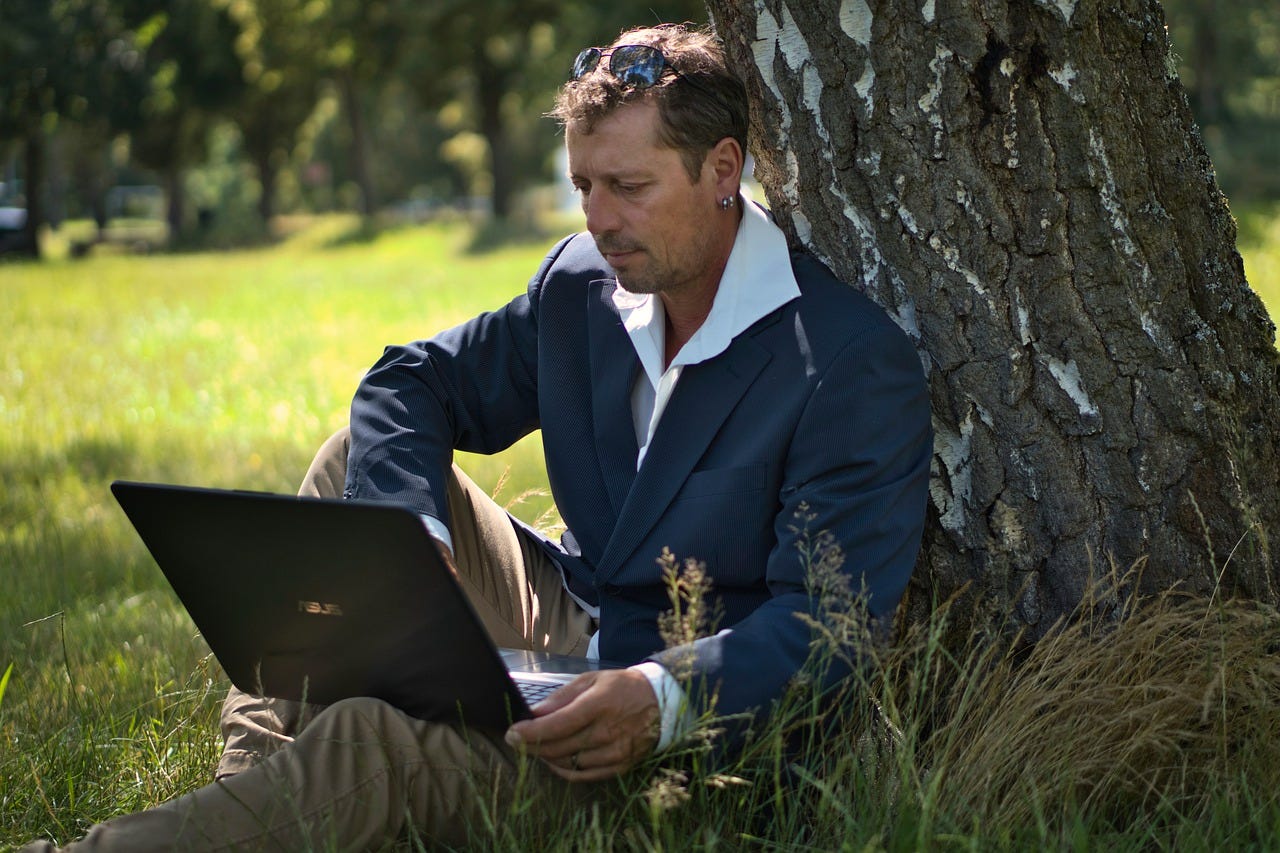 A man sitting by a tree and doing work which demonstrates work life integration instead of work life balance.