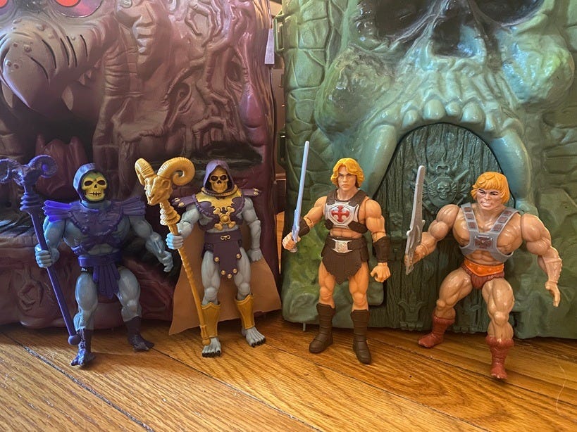 Vintage 1980s Skeletor and He-Man stand beside their 2026 counterparts in front of vintage Snake Mountain and Castle Grayskull playsets. Vintage 1980s Skeletor and He-Man stand beside their 2026 counterparts in front of vintage Snake Mountain and Castle Grayskull playsets.