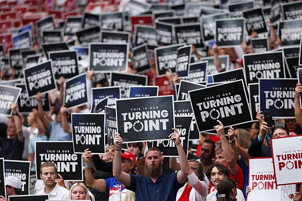 Attendees hold up Turning Point USA signs at the memorial service for political activist Charlie Kirk at State Farm Stadium on September 21, 2025 in...