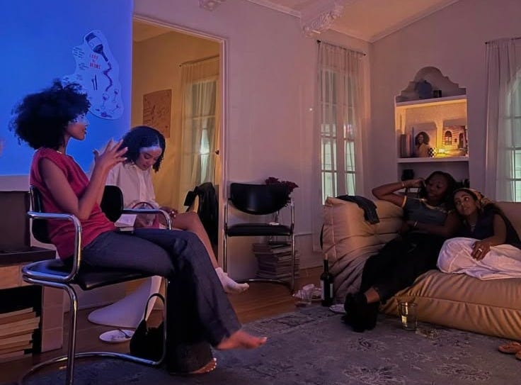 This may contain: three women sitting on couches in a living room watching something on the tv screen