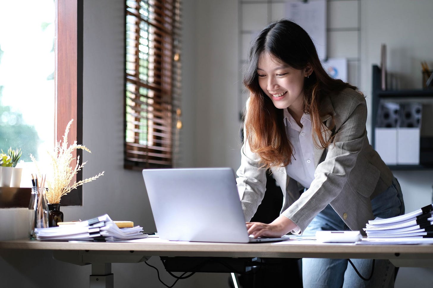 A young woman typing on laptop while standing