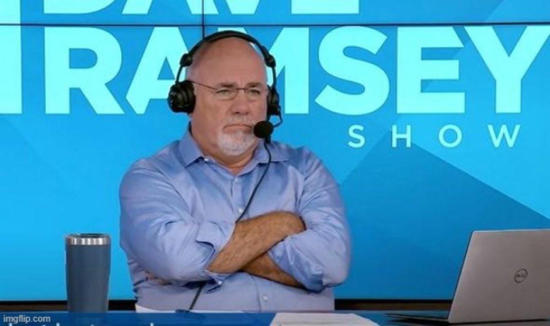 Man with glasses and white beard wearing light blue shirt and headphones sits with arms crossed looking serious in studio setting. Blue background displays Dave Ramsey Show text in white letters. Desk holds silver tumbler laptop and papers. Man with glasses and white beard wearing light blue shirt and headphones sits with arms crossed looking serious in studio setting. Blue background displays Dave Ramsey Show text in white letters. Desk holds silver tumbler laptop and papers.