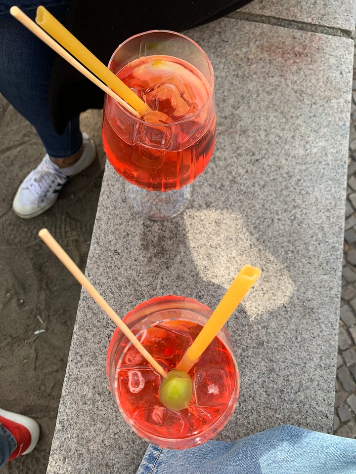 top left to bottom right: image of two spring raspberry colored cocktails with olives and a thick tubular pasta "straw", containers of white asparagus for sale at 12.99Euro per kilo, barlauch gnocchi (green)with price, cheerful red Karl'sStrawberries kiosk