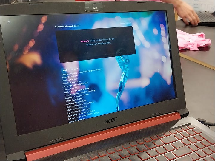 An image of a screen showing kareoke lyrics, and a creepy doll-like human figure