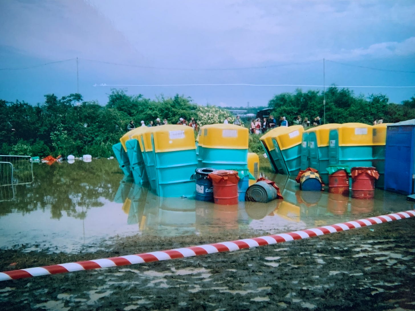 Photograph of a group of chemical toilets and dustbins half submerged in water and mud