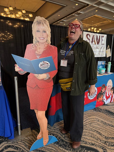 Woman standing next to a Dolly Parton cut out, cover of a zine and view from the table
