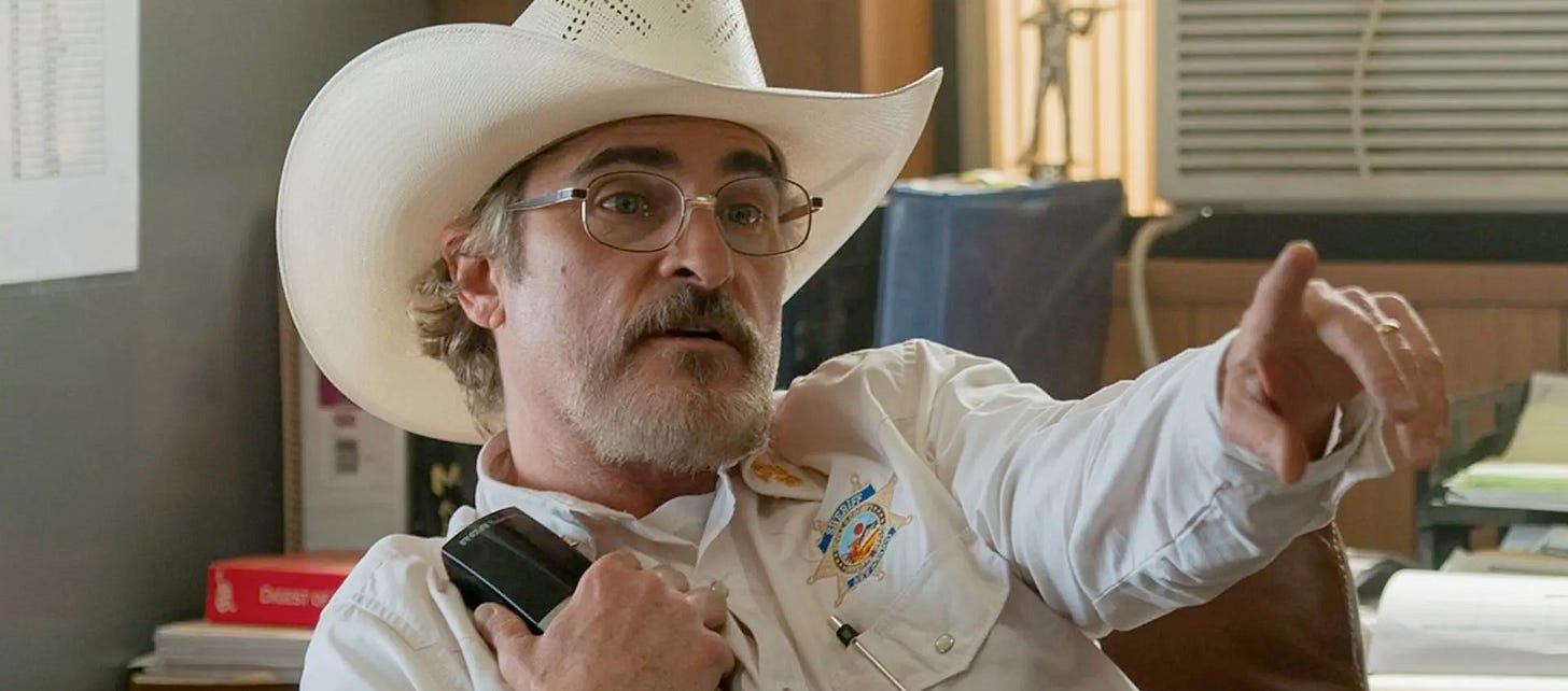 Joaquin Phoenix as Sherrif Joe Cross, at his desk in Stetson hat, holding the phone against his chest and pointing across the room assertively