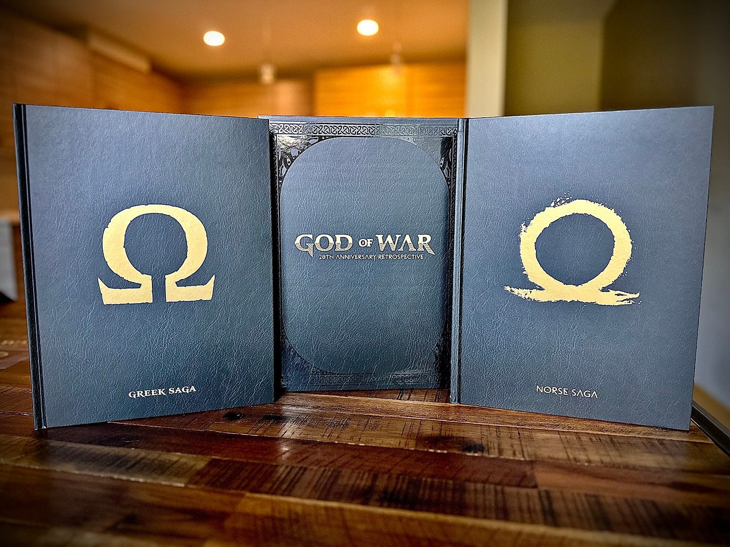 The 20th anniversary retrospective God of war books, 2 books set a top of wooden table one that says Greek saga the other that says Norse Saga
