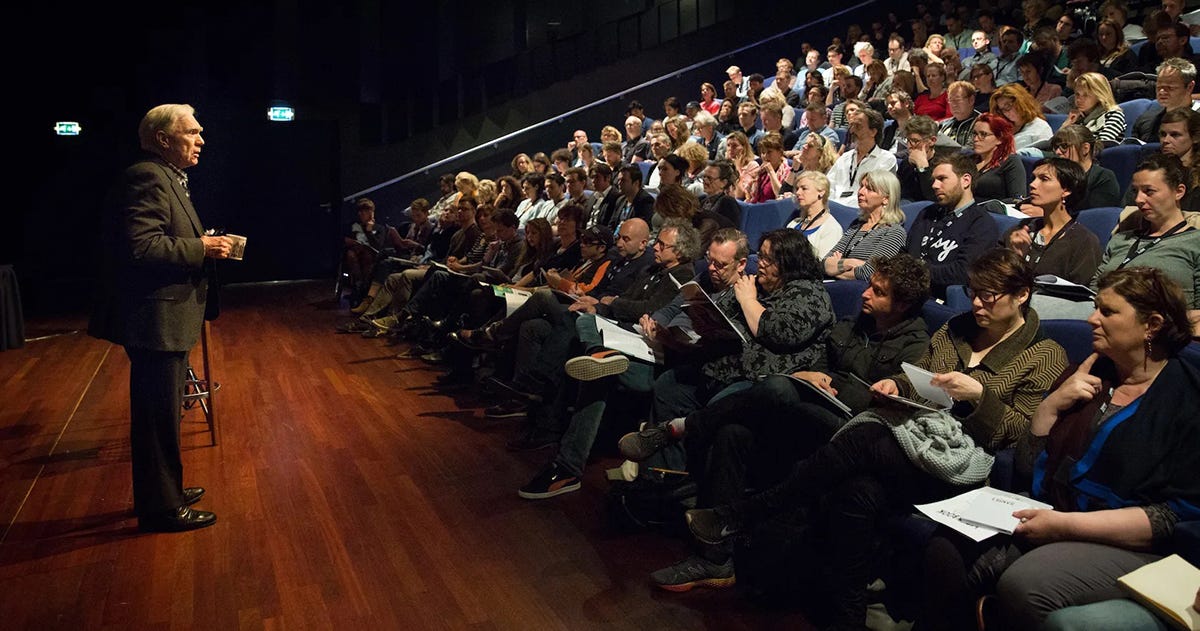 A person standing in front of a group of people sitting in chairs

Description automatically generated with low confidence