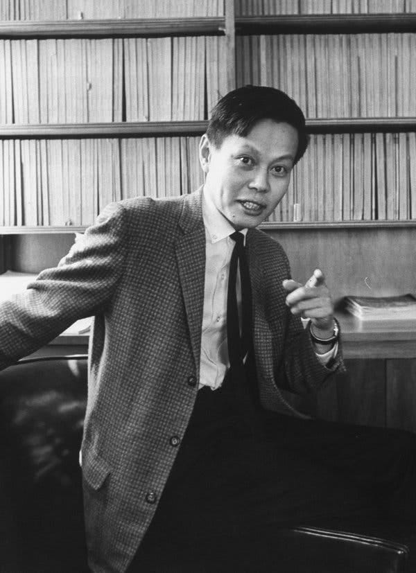A young man in a checkered sports coat, he looks at the camera and points his finger in a black-and-white photo.