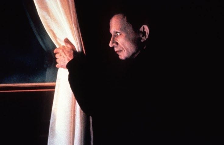 This may contain: an older man looking out the window with his hand on the curtain and staring into the distance