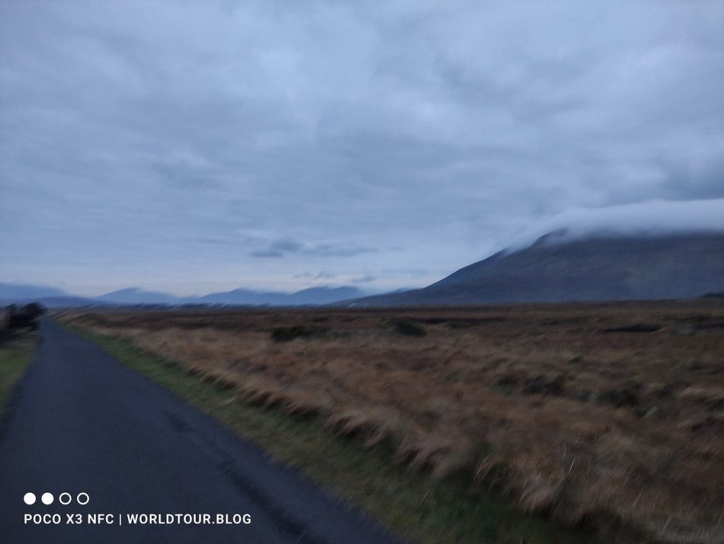 Path continues, cloud-shrouded mountain behind a field to the right