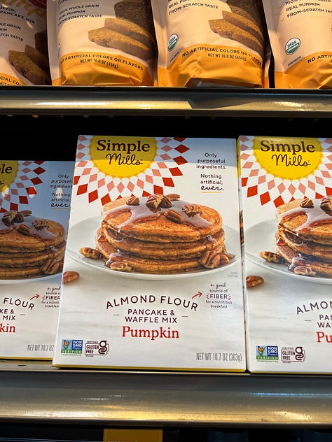 A grid of six photos of pumpkin-flavored products on shelves at an American Whole Foods: pumpkin spice grain-free cereal, pumpkin spice popcorn, pumpkin spice oat milk, cans of pumpkin chai hard tea, pumpkin spice oat bites and a pumpkin almond flour pancake mix.