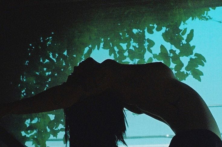 This may contain: a woman standing in front of a tree with her head tilted to the side and hands behind her back