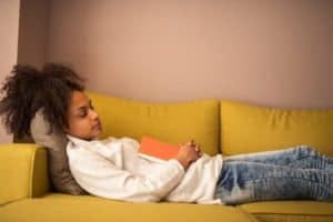 An young woman napping on the couch with a book in hand. By bernard bodo/istock
