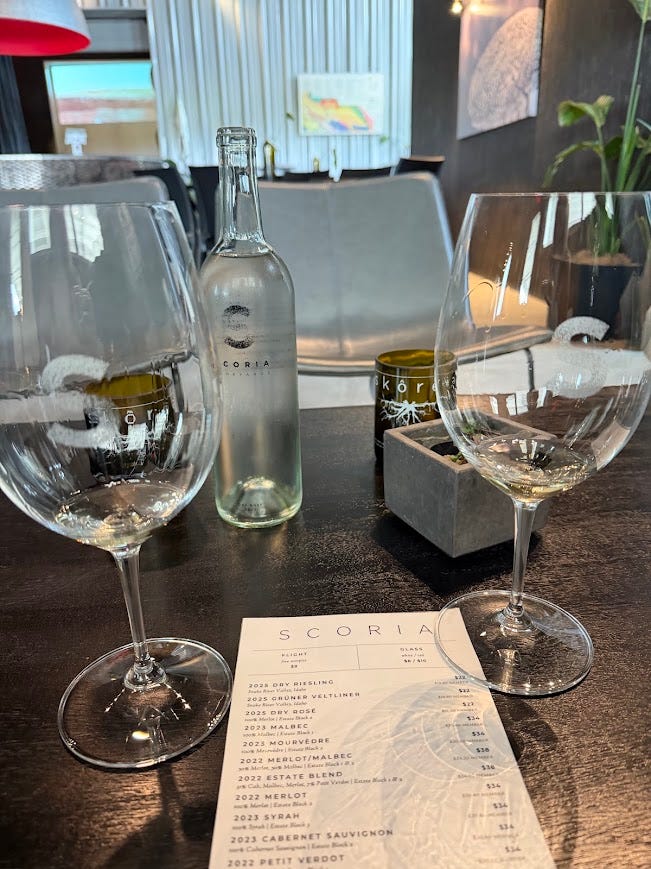 Two glasses of white wine and a bottle of Scoria dry Riesling on a tasting room table, next to the Scoria wine list menu.
