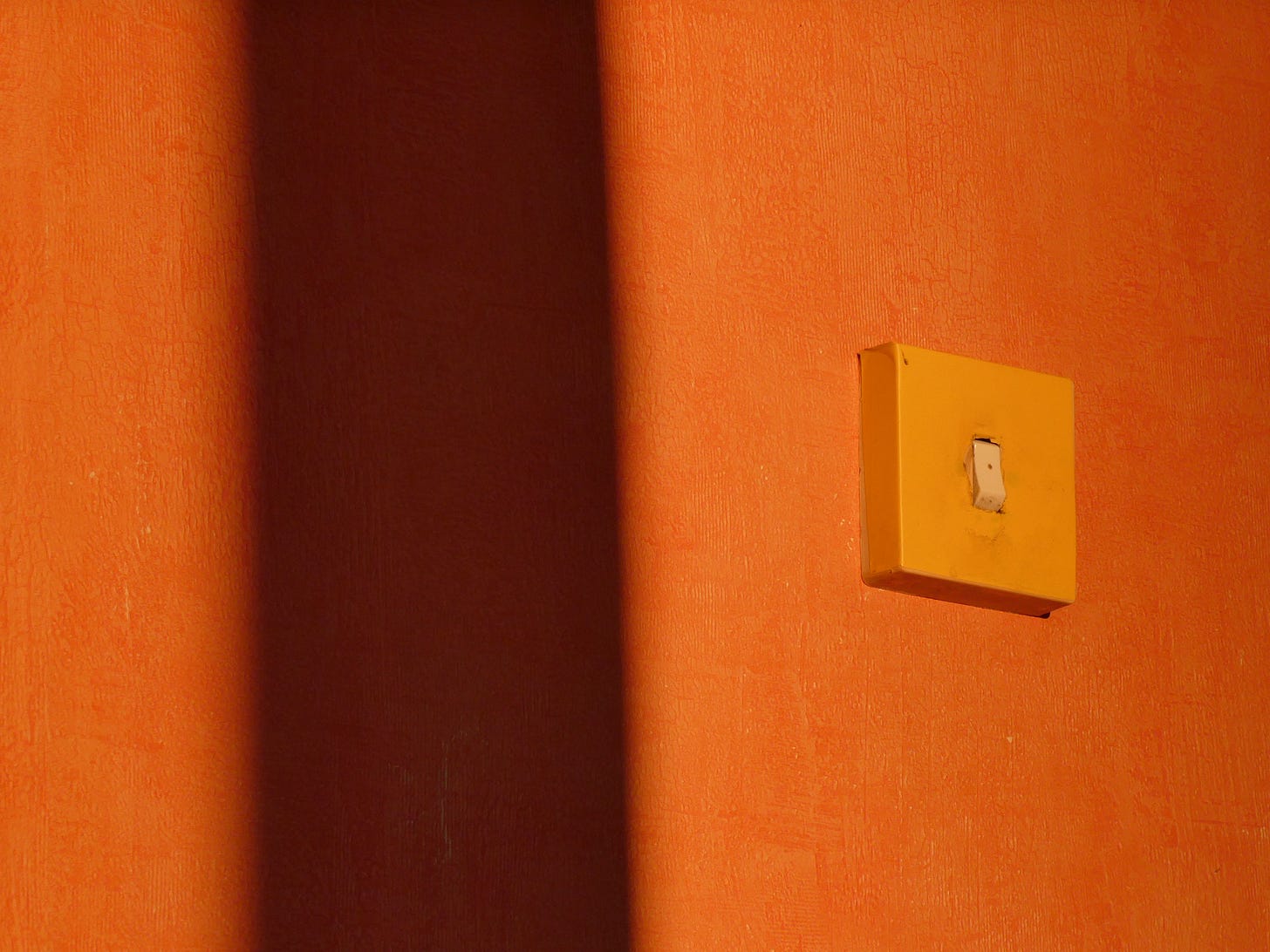 Minimalist image showcasing a light switch casting shadows on a vibrant orange wall. Minimalist image showcasing a light switch casting shadows on a vibrant orange wall.