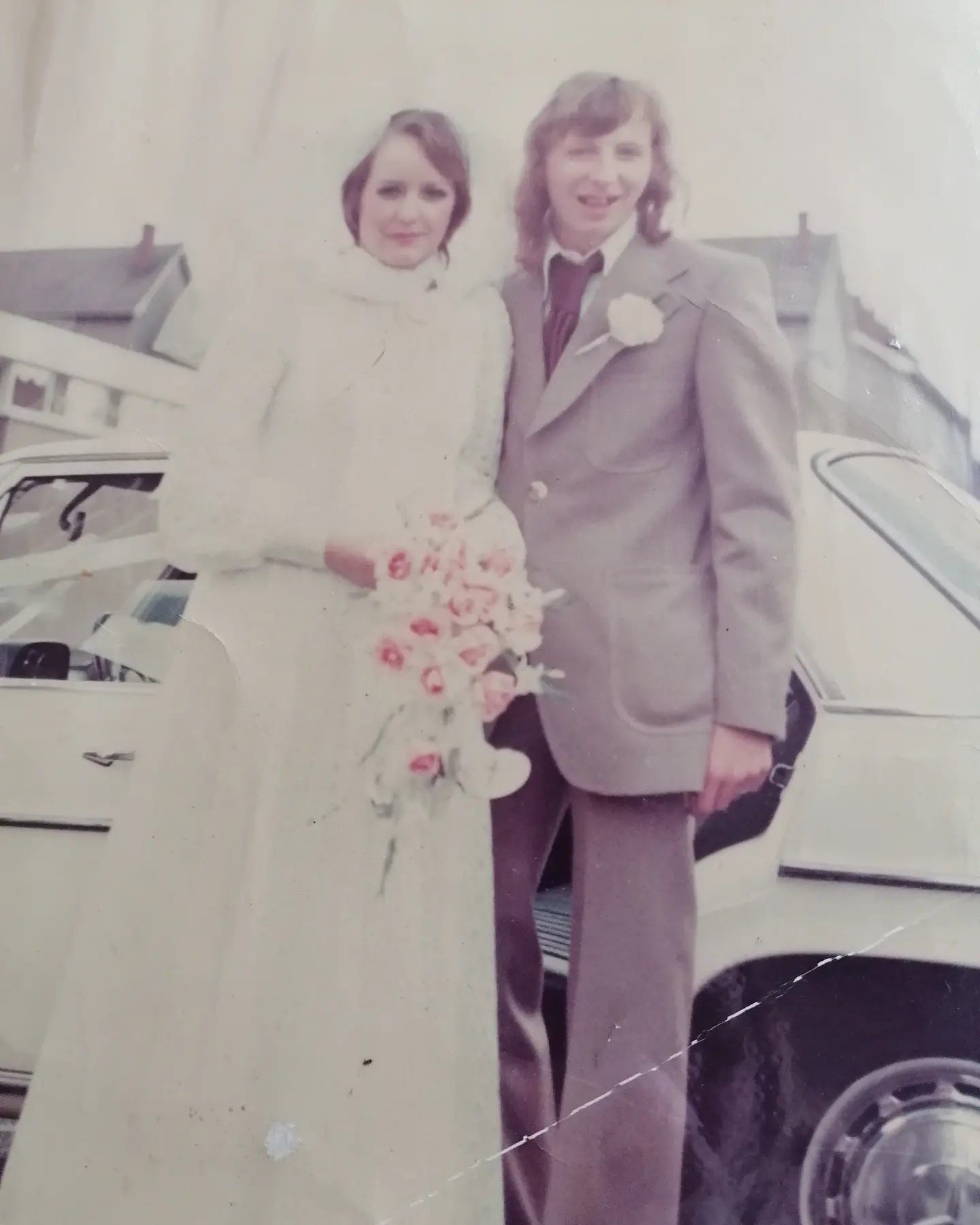 a faded wedding shot of a young women in white holding pink roses and a young man with long hair in a light brown suit a faded wedding shot of a young women in white holding pink roses and a young man with long hair in a light brown suit