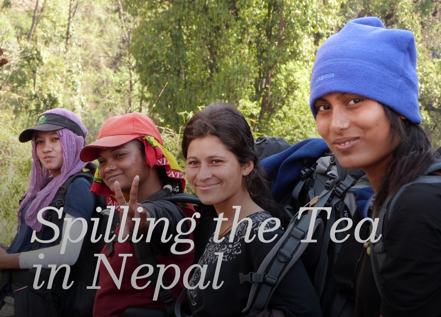 Close up of four young Nepali women, looking at the camera and smiling. Three are wearing head coverings, all are wearing dark clothing.