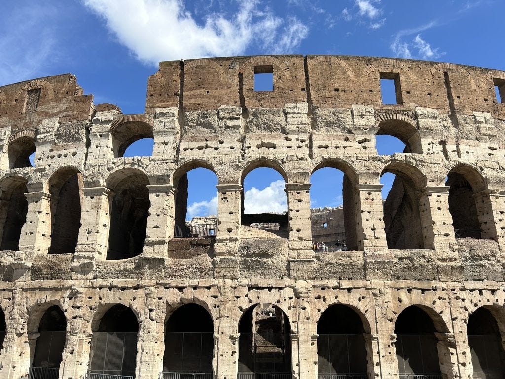 Exterior of the Colosseum in Rome showing columns and blue sky.