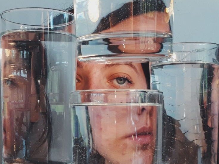 This may contain: a woman's face is reflected in several glass vases with water on them This may contain: a woman's face is reflected in several glass vases with water on them