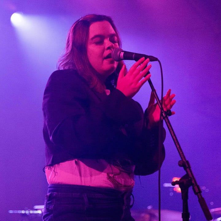Two purple hued photos of Maye performing live in 2022.