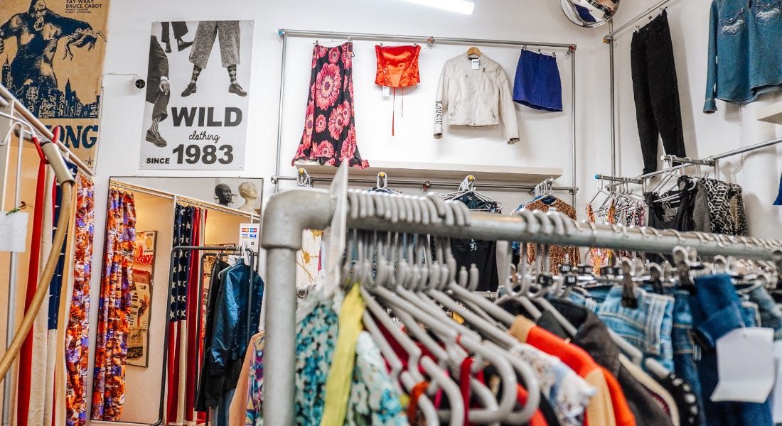 A clothes rail with colourful clothes on it, with a wall of posters and clothes behind it