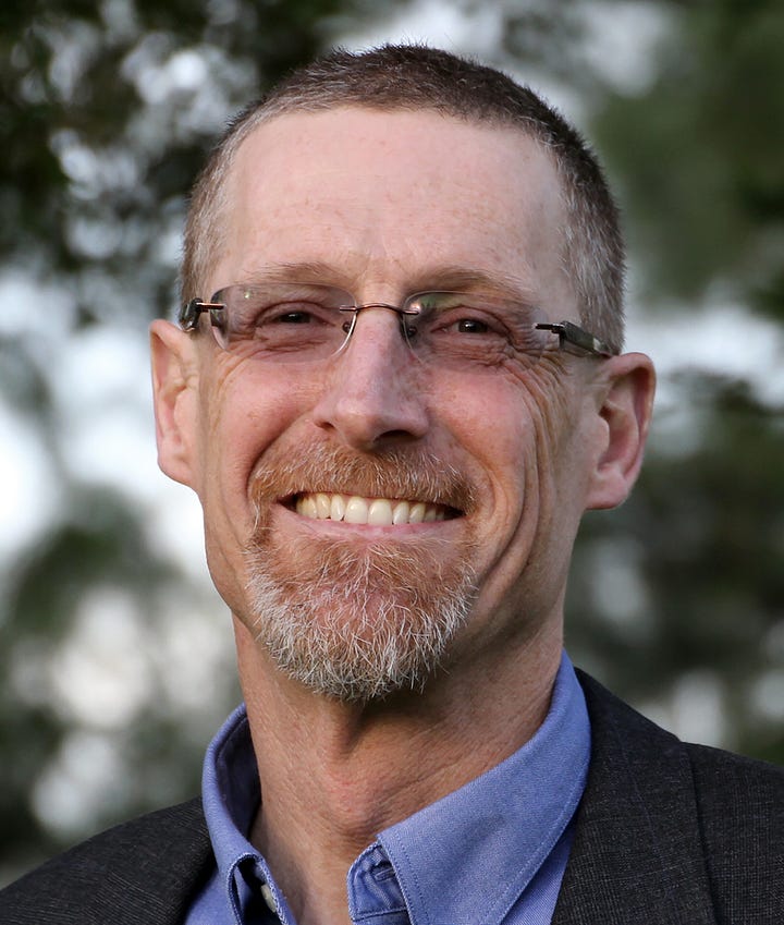 Two men in their fifties, both wearing glasses and collared shirts.