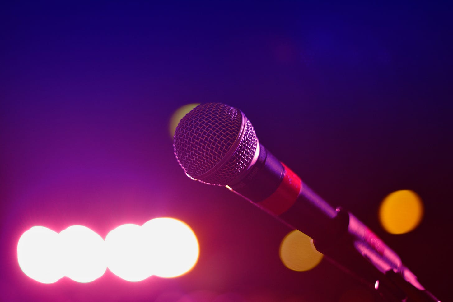 a black microphone with a red band clipped on a stand in a room with pink blue and yellow lights