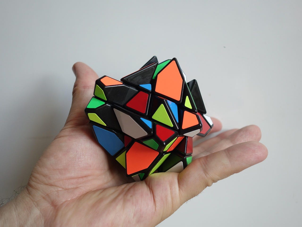 A hand holds a colorful logic puzzle that looks like an altered form of a rubik's cube.