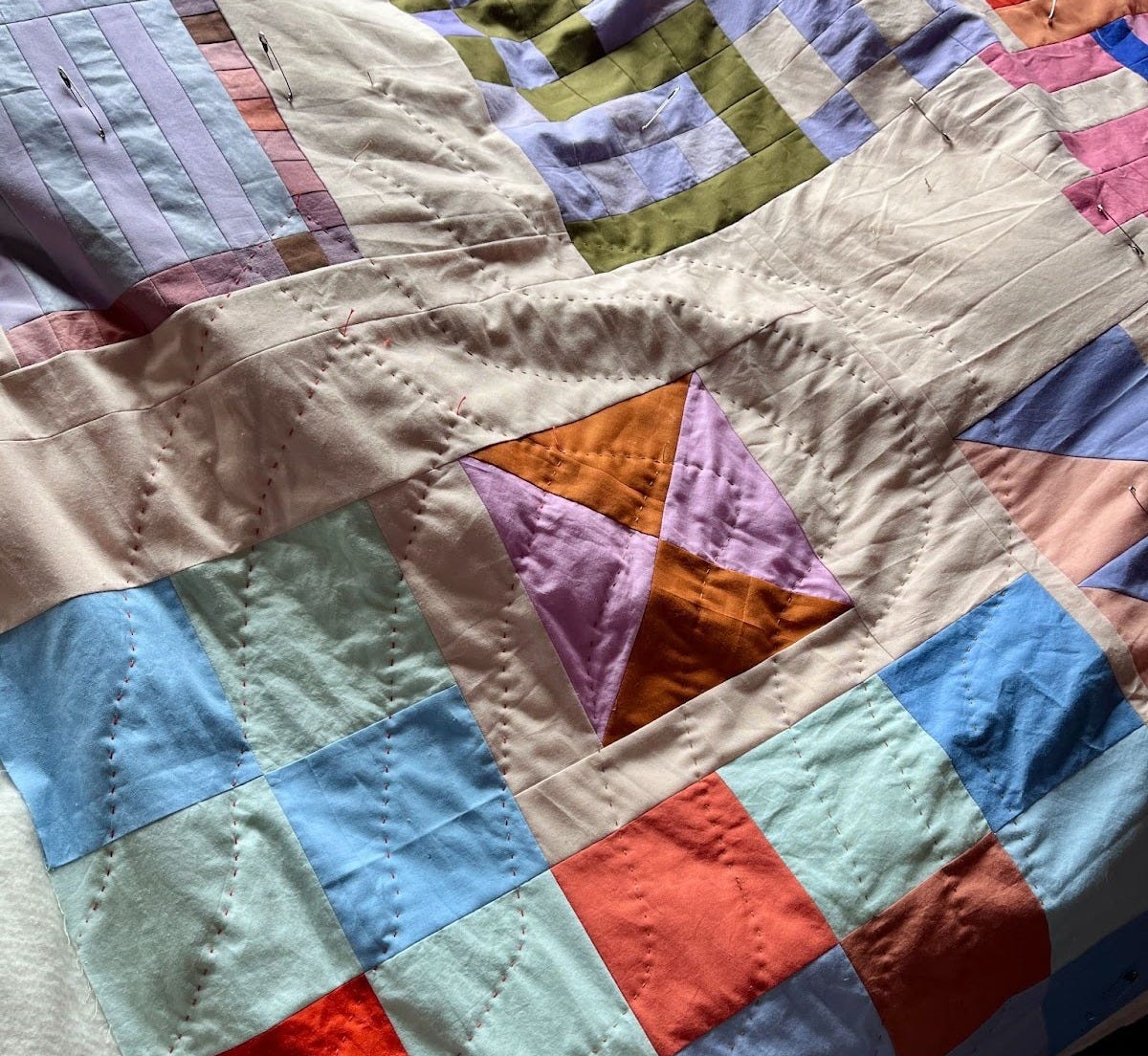 A close up of the quilt being hand stitched. The lines are stitched in a running stitch, in fluid parallel lines each approximately 4 inches apart from each other. A close up of the quilt being hand stitched. The lines are stitched in a running stitch, in fluid parallel lines each approximately 4 inches apart from each other.
