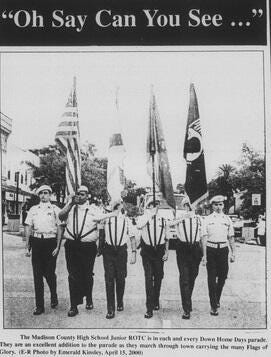 High school ROTC color guard marching in a parade, carrying multiple flags under the heading “Oh Say Can You See …” High school ROTC color guard marching in a parade, carrying multiple flags under the heading “Oh Say Can You See …”