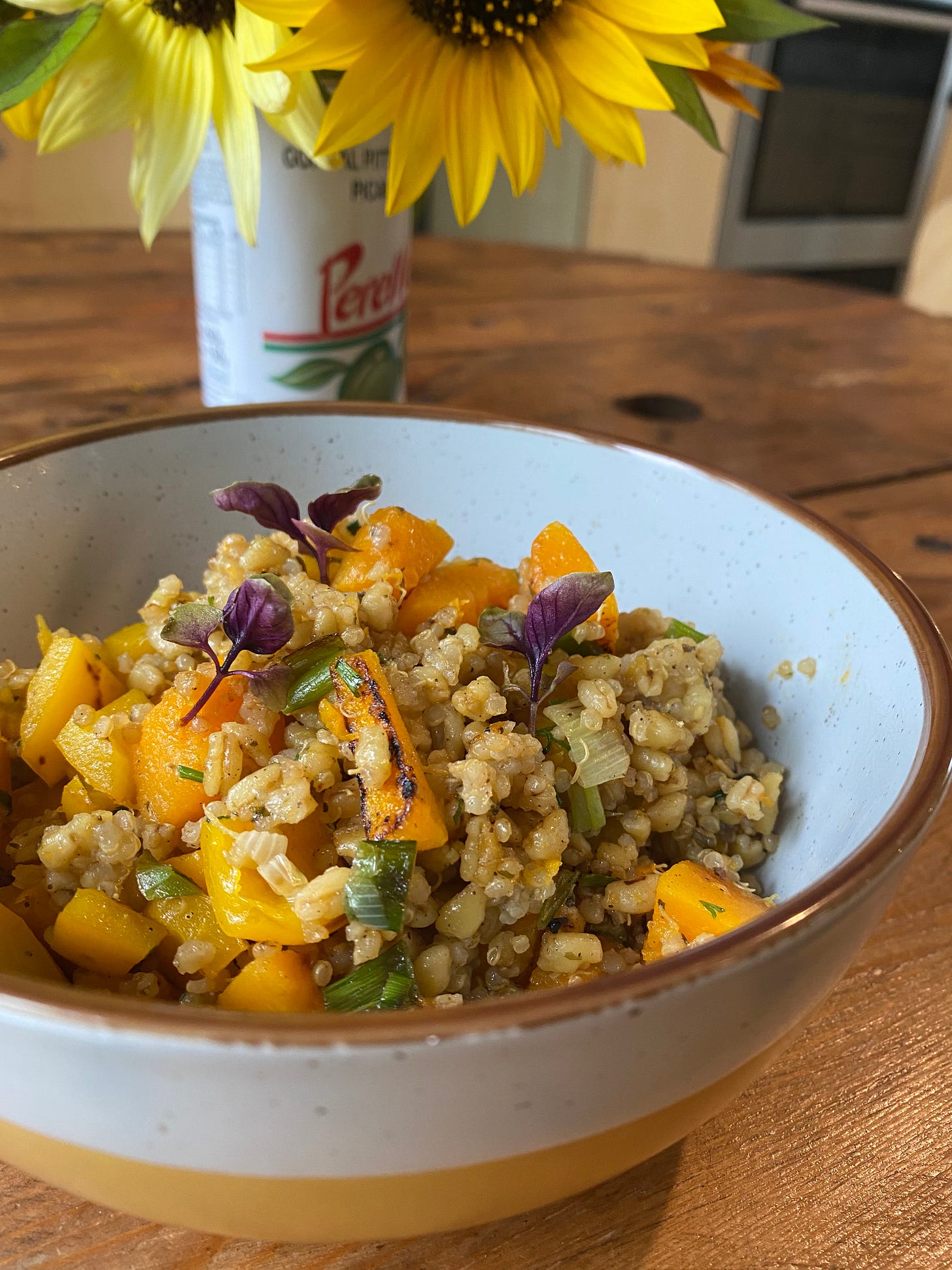 Bowl of grains and vegetables on a table in front of sunflowers in a tin.