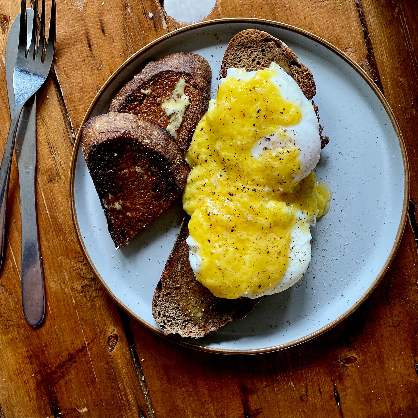 Eggs benedict on toast with bright yellow hollandaise sauce, served on a white and yellow plate on a wooden table.