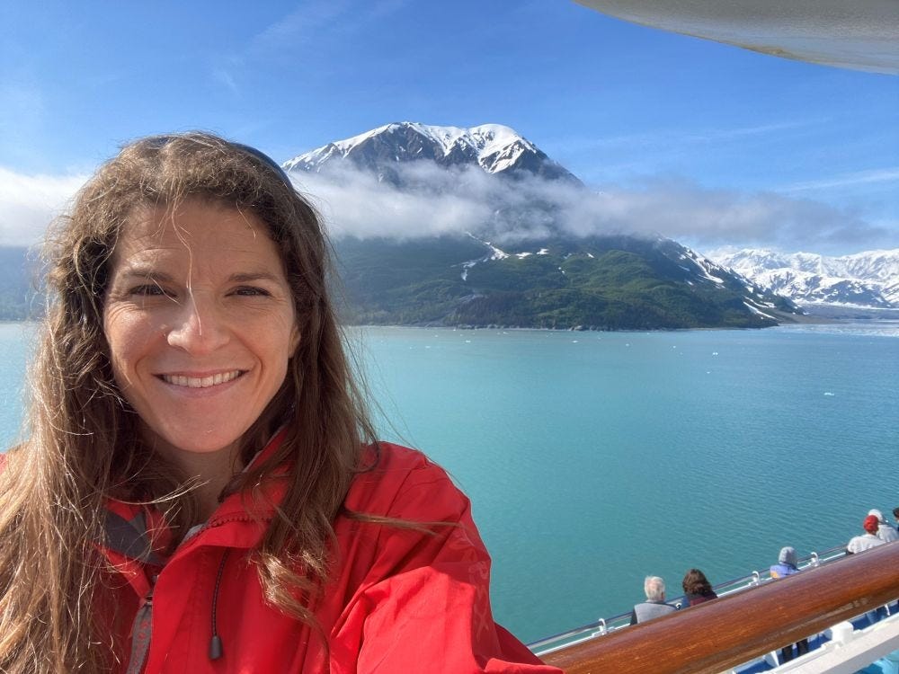 a woman on the top deck of a cruise ship in Alaska with beautiful snow capped mountains and glaciers in the distance. a woman on the top deck of a cruise ship in Alaska with beautiful snow capped mountains and glaciers in the distance.