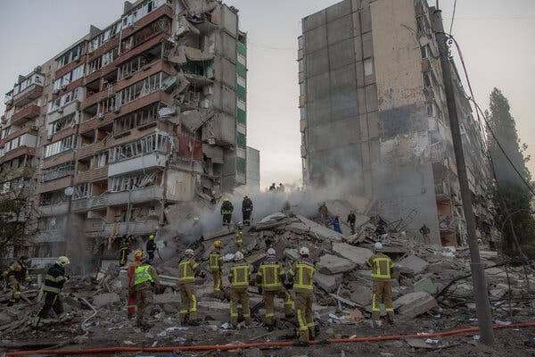 Two heavily damaged building by a pile of smoking rubble. Rescue workers stand around and on the rubble. Two heavily damaged building by a pile of smoking rubble. Rescue workers stand around and on the rubble.