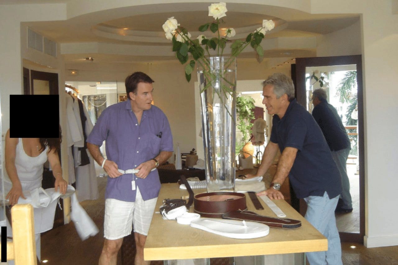 Peter Mandelson adjusting a belt he is wearing while Jeffrey Epstein is smiling and a woman whose face is redacted is nearby