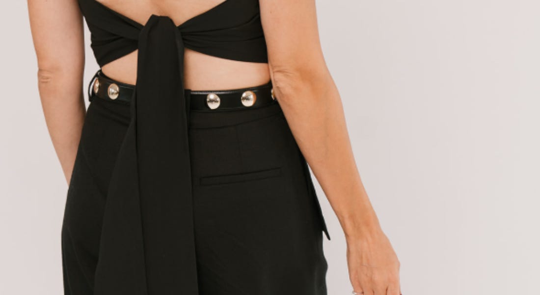 A woman wearing a black tie-back top and black trousers with a studded belt A woman wearing a black tie-back top and black trousers with a studded belt